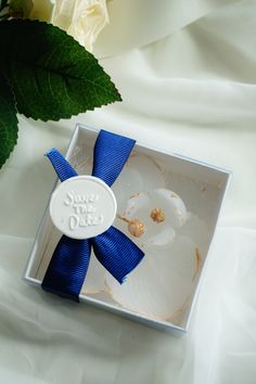 a white rose with a blue ribbon in a small gift box on a white sheet