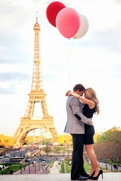 a man and woman kissing in front of the eiffel tower with two balloons