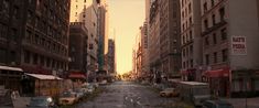 an empty city street with cars parked on both sides and tall buildings in the background