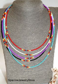 a necklace with multi colored beads on a mannequinl stand next to a seashell