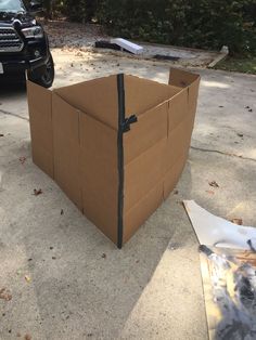 an open cardboard box sitting on the ground next to a parked car in front of it