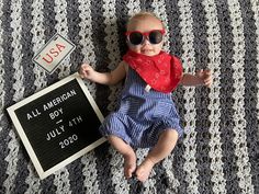 a baby wearing sunglasses is laying on a blanket with a sign that says, all american boy july 4th