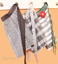 several different types of scarves hanging from hooks on a wall with the same fabric