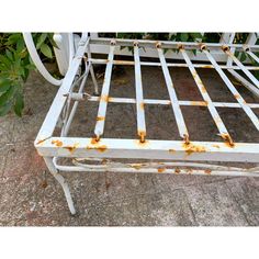 an old white metal bed frame with rust on the bottom and foot board is sitting in front of some bushes