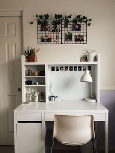 a white desk and chair in a room with plants on the wall above it, next to a door