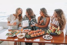 three women sitting at a table with food on it and drinks in front of them