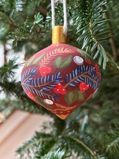 a red ornament hanging from a tree filled with green leaves and berries on it's side