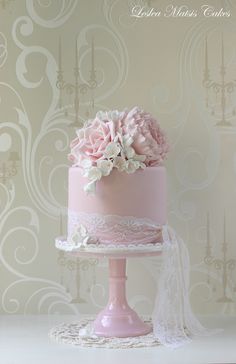 a pink cake with white flowers and lace on the top is sitting on a table