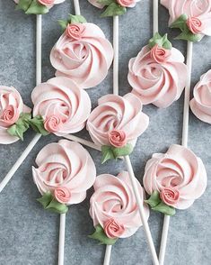 pink frosted roses are on top of white lollipops with green leaves