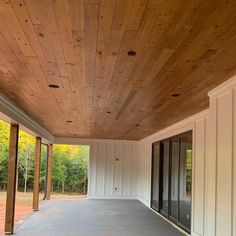 an empty covered porch with sliding glass doors and wood paneling on the ceiling is seen in this image