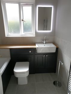 a white toilet sitting next to a bath tub in a bathroom under two large windows