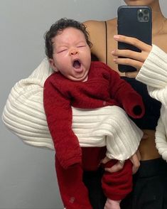 a woman holding a baby in her arms and taking a selfie with the phone