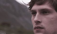 a close up of a person wearing a suit and tie with mountains in the background