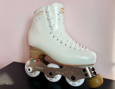 a pair of white roller skates sitting on top of a black table next to a pink wall