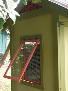 a small green house with a red window on the side and a bird feeder in it