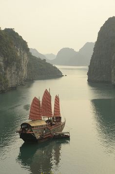 a boat floating on top of a large body of water next to tall mountains in the distance