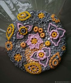 a crocheted doily with yellow and pink flowers in the center on a black surface