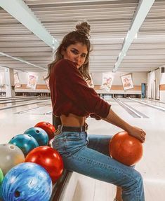 a woman sitting on a bowling alley with her legs crossed and balls in front of her