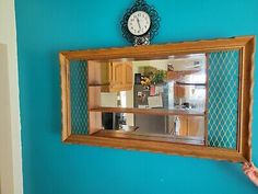 a mirror hanging on the wall with a clock above it and a hand reaching up to take a photo