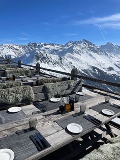 a wooden table topped with plates covered in hay on top of a snow covered mountain