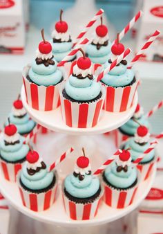 cupcakes with blue frosting and cherries on top are arranged in red and white striped paper