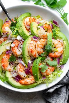 a salad with shrimp, avocado and cilantro in a white bowl