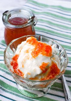 a glass bowl filled with ice cream and sauce next to a jar full of jelly