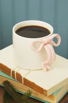 a cup of coffee sitting on top of an open book next to a pine branch