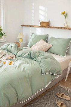 a bed with green comforter and pillows in a white room next to a window