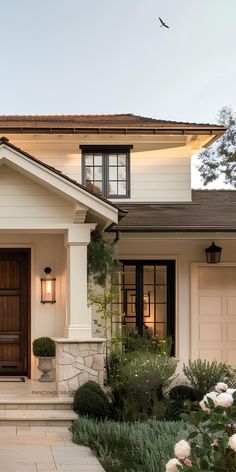 the front entrance to a house with white flowers and bushes in front of it on a sunny day