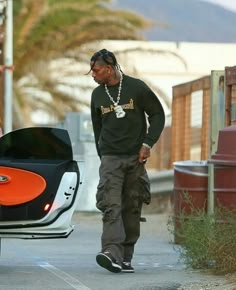 a man walking down the street next to an orange and black car