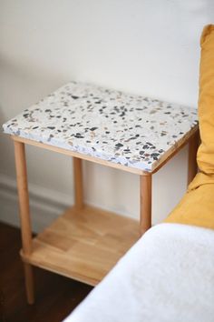 a small white table sitting next to a bed with yellow pillows on top of it