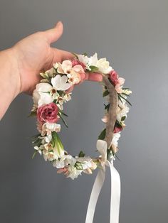 a hand holding a flower wreath with white ribbon around it and flowers in the middle