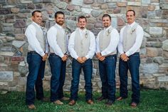 a group of men standing next to each other in front of a stone wall and grass