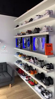 a room filled with lots of shoes on shelves next to a gray couch and chair