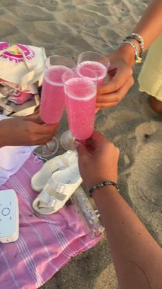 three people toasting with pink drinks on the beach