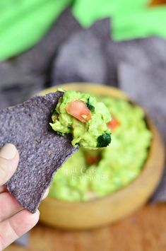 a hand holding a tortilla chip with guacamole in the background