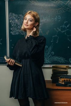 a woman standing in front of a chalkboard holding a book and looking at the camera