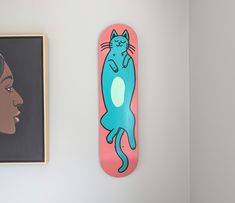 a skateboard with a blue cat on it next to a framed photograph and a woman's face