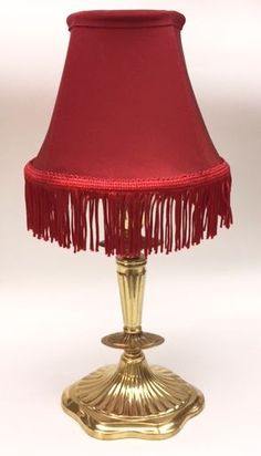 a gold lamp with red shade and fringed lampshade on the bottom side