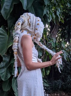 a woman in a white dress is wearing a crocheted head scarf and holding her hands out