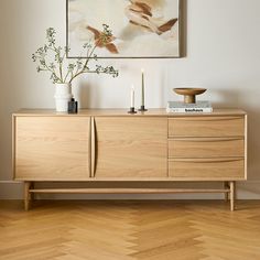 a wooden sideboard with candles and flowers on it in front of a framed painting