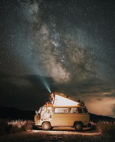 a van is parked under the night sky with its lights on and stars above it