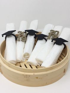 a group of white napkins with black graduation caps on them in a bamboo steamer