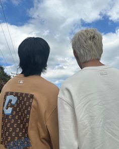 two people standing next to each other looking at the blue sky with clouds in the background