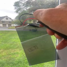 a hand holding a piece of paper with a wire attached to it, in front of a window