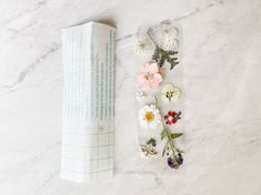 some flowers are laying next to an open book on a white marble counter top,