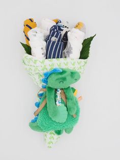 a green stuffed animal sitting in a paper bag filled with baby clothes and other items