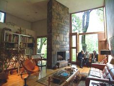 two people sitting in a living room with large windows looking out onto the trees outside