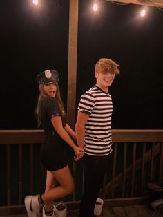 two people standing on a deck holding hands and smiling at each other with lights in the background